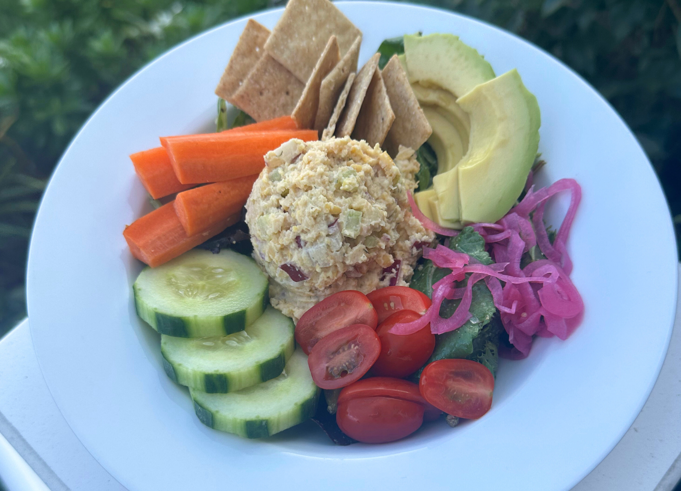 Vegan tuna salad served on a bed of lettuce with crackers, avocado, cucumbers, carrots, tomatoes and pickled onions.
